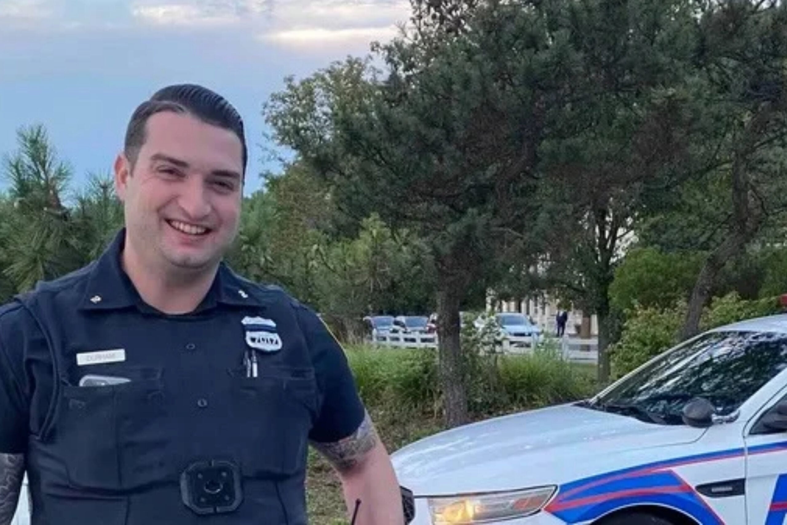 Photo of Officer Chris Durham in police uniform near police car.