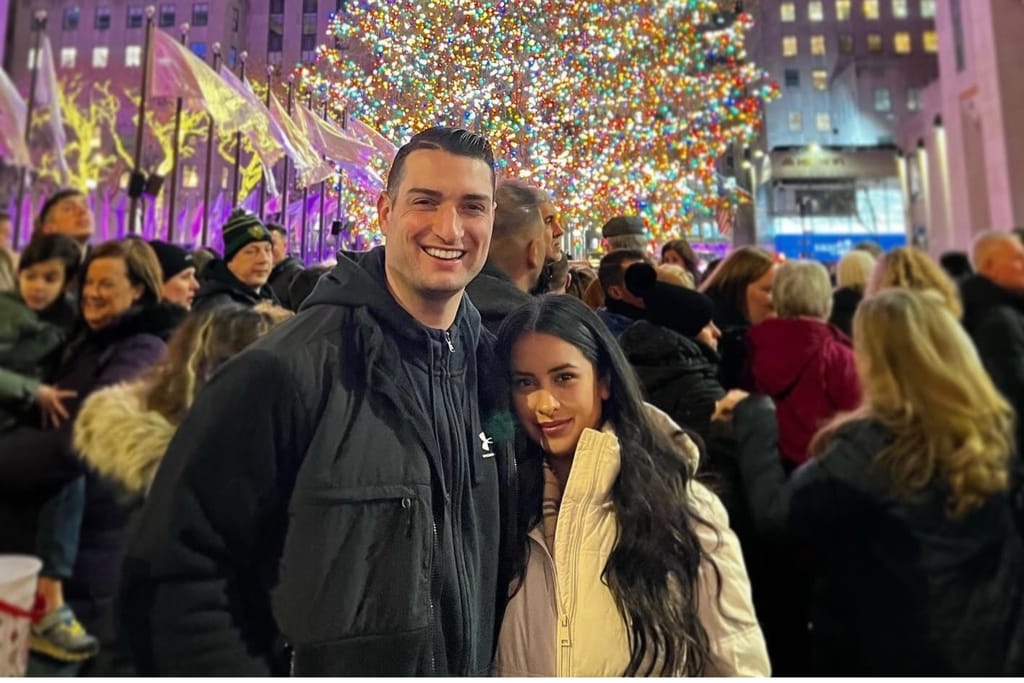 Chris Durham and Carolyn Infantas smiling and posing whilst standing in front of lighted Christmas tree in Manhattan.