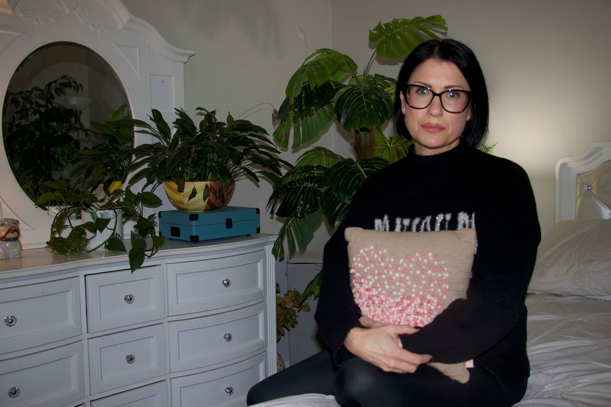 A woman sits on a bed with a pillow.